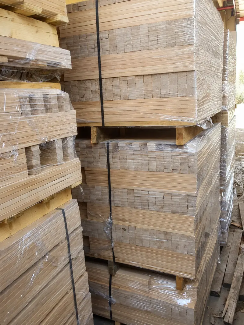 Foil-wrapped and strapped packs of beech bed-slat elements stacked in the yard