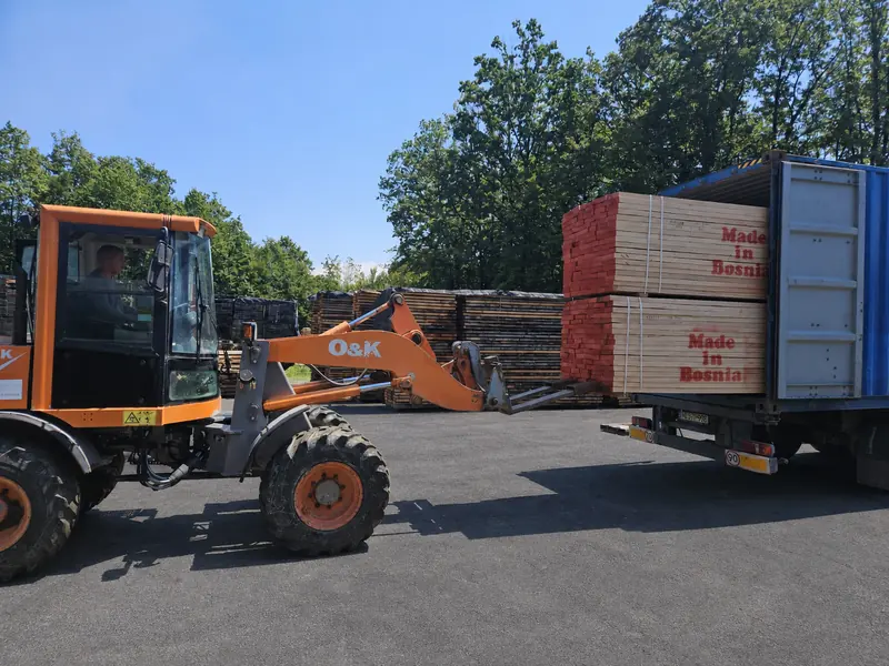 A wheel loader lifting a Made in Bosnia timber pack into a shipping container on a trailer