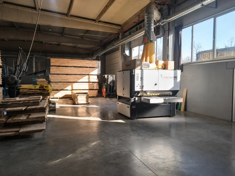 Production hall with an extraction-hooded machine and stacked pallets in morning light