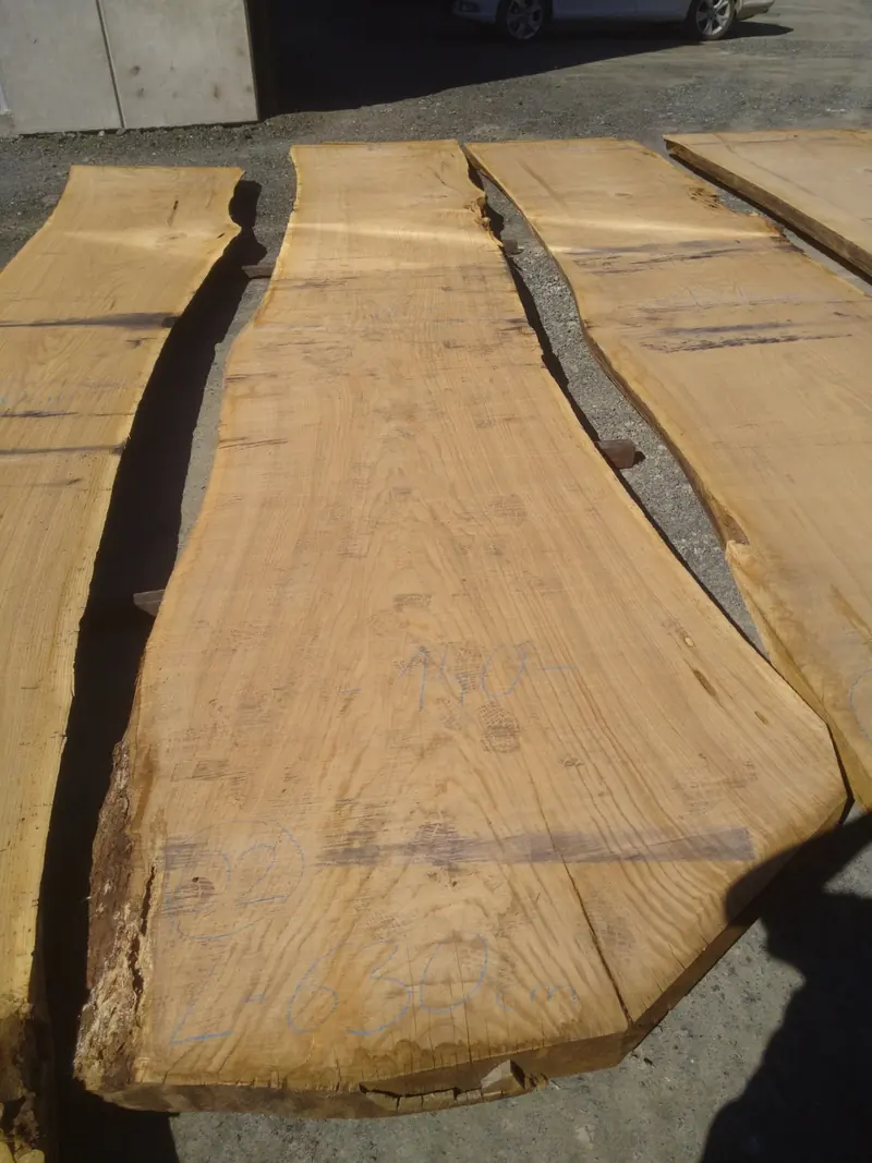 Three wide live-edge oak slabs seen close up, showing the natural edge and shakes