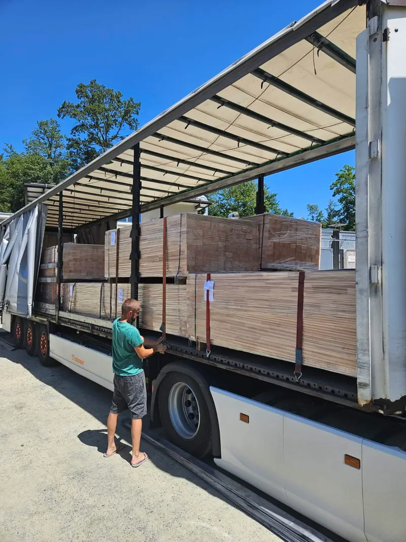 Mitarbeiter prüft eine umreifte Ladung verleimter Platten auf einem Pritschenanhänger