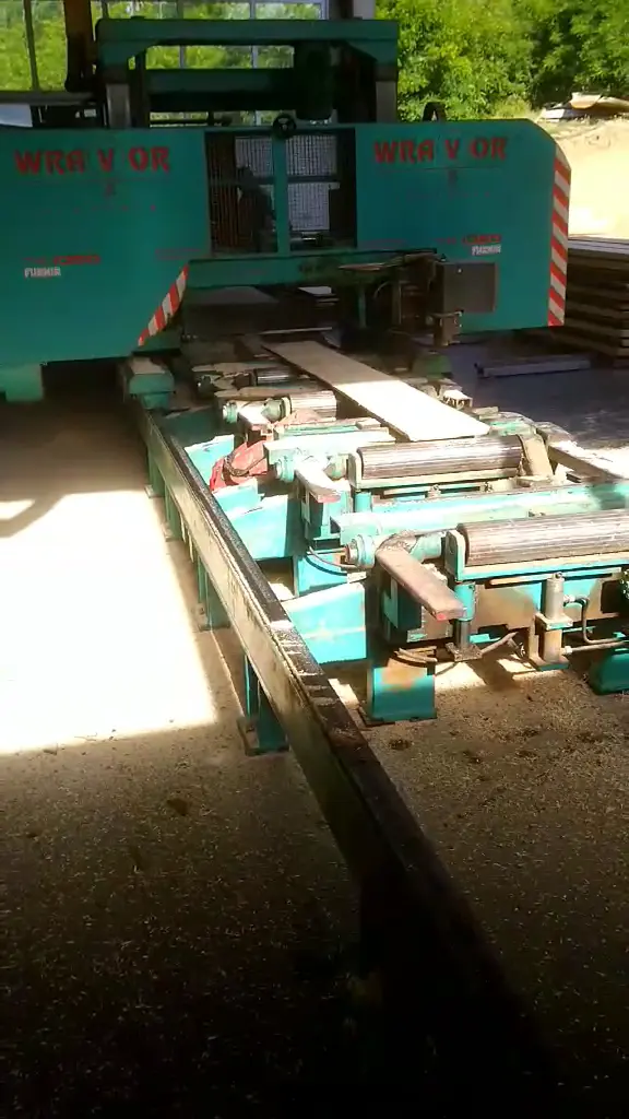 The multi-blade log saw and its roller conveyor in the open-sided sawing hall