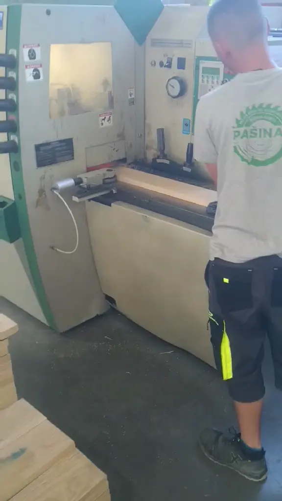 An operator working at the planing machine with planed beech elements stacked in front